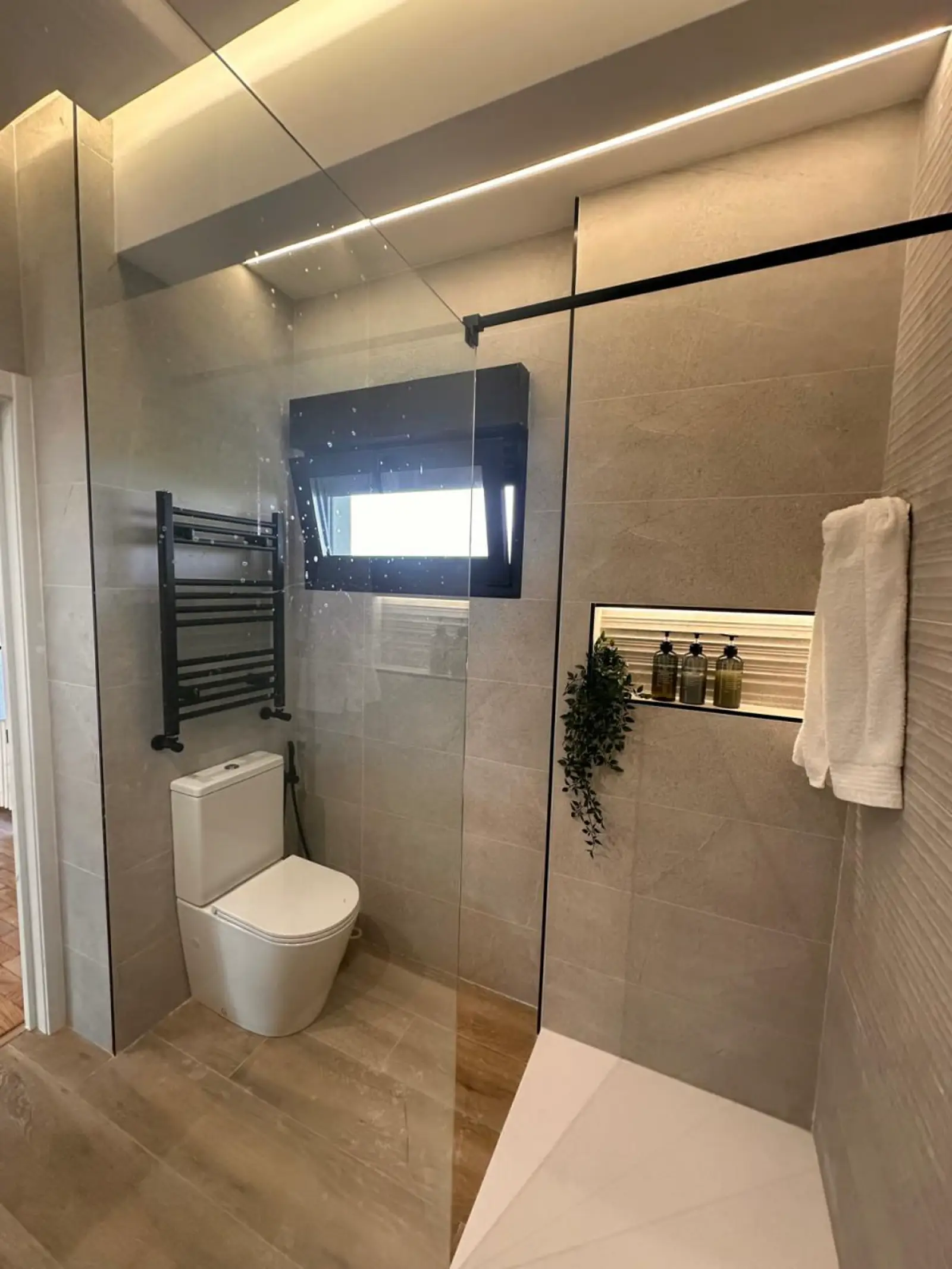 Baño reformado con mampara de cristal, radiador negro, hornacina y plato de ducha